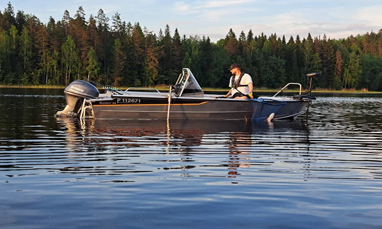 Ammattimainen Buster-kalastusvene upeissa Saimaan maisemissa, kalastaja väsyttämässä kalaa.