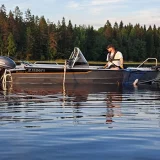 Ammattimainen Buster-kalastusvene upeissa Saimaan maisemissa, kalastaja väsyttämässä kalaa.